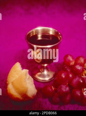 Ein Kelch gefüllt mit Rotwein, Trauben und Brot, der die Kommunion der katholischen Religion darstellt Stockfoto