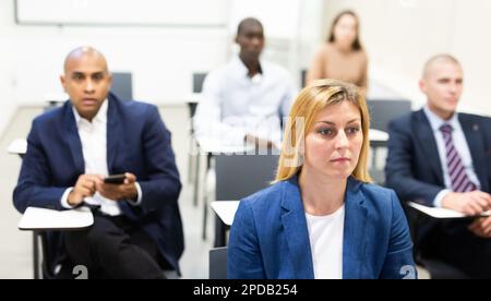 Aufmerksame Frau, umgeben von Kollegen, die sich die Präsentation im Konferenzraum anhören Stockfoto