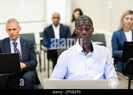 Ein Geschäftsmann, der während eines Seminars an einem Laptop arbeitet Stockfoto