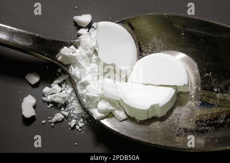 Pharmazeutisches Arzneimittelpulver auf einem silbernen Metalllöffel. Zerschmettertes Mittel, Tabletten, oben auf einem grauen Tisch im Hintergrund. Stockfoto