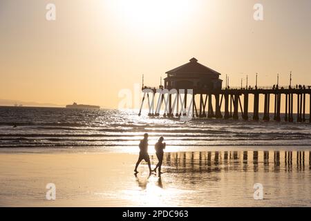 Ein paar Spaziergänge am Strand vor dem Pier am Huntington Beach, Kalifornien bei Sonnenuntergang Stockfoto