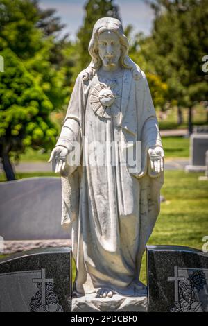 Eine Steinstatue Jesu Christi, die seine Hände ausstreckt, die auf einem Grabstein des Friedhofs befestigt ist Stockfoto