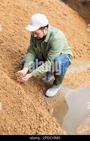 Bauer hockt auf einem großen Haufen verbrauchten Getreides der Brauerei Stockfoto