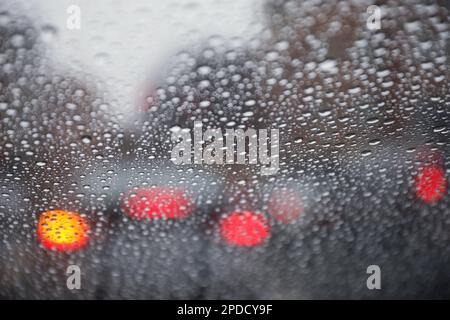 Regentropfen auf einem Fenster mit einer sanft verschwommenen Stadtlandschaft dahinter, die eine stimmungsvolle, atmosphärische Szene erzeugen. Ideal für Wetter, melancholische, gemütliche Momente in Innenräumen, Stockfoto