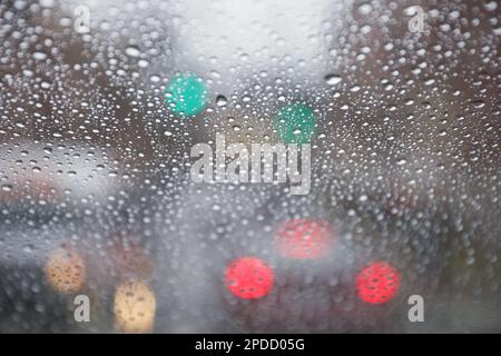 Regentropfen auf einem Fenster mit einer sanft verschwommenen Stadtlandschaft dahinter, die eine stimmungsvolle, atmosphärische Szene erzeugen. Ideal für Wetter, melancholische, gemütliche Momente in Innenräumen, Stockfoto
