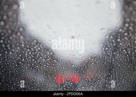 Regentropfen auf einem Fenster mit einer sanft verschwommenen Stadtlandschaft dahinter, die eine stimmungsvolle, atmosphärische Szene erzeugen. Ideal für Wetter, melancholische, gemütliche Momente in Innenräumen, Stockfoto