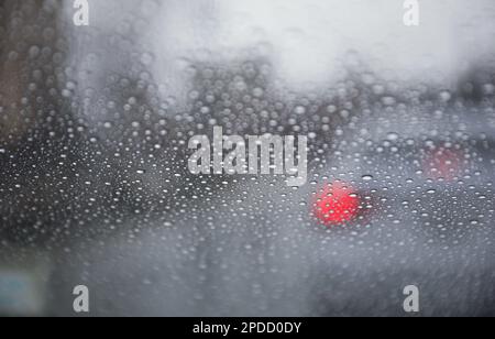 Regentropfen auf einem Fenster mit einer sanft verschwommenen Stadtlandschaft dahinter, die eine stimmungsvolle, atmosphärische Szene erzeugen. Ideal für Wetter, melancholische, gemütliche Momente in Innenräumen, Stockfoto