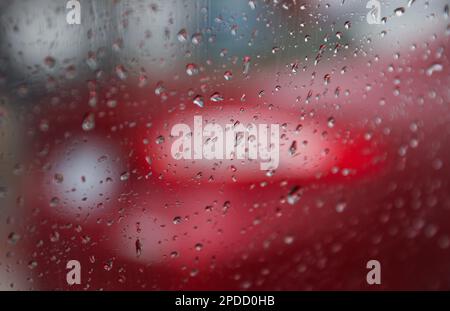 Regentropfen auf einem Fenster mit einer sanft verschwommenen Stadtlandschaft dahinter, die eine stimmungsvolle, atmosphärische Szene erzeugen. Ideal für Wetter, melancholische, gemütliche Momente in Innenräumen, Stockfoto