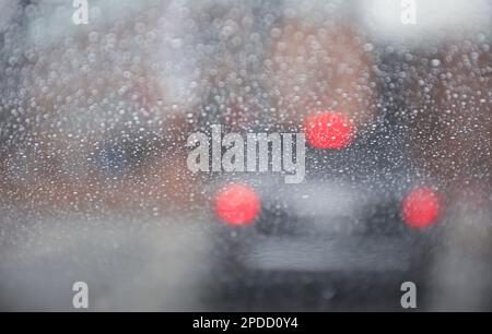 Regentropfen auf einem Fenster mit einer sanft verschwommenen Stadtlandschaft dahinter, die eine stimmungsvolle, atmosphärische Szene erzeugen. Ideal für Wetter, melancholische, gemütliche Momente in Innenräumen, Stockfoto