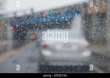Regentropfen auf einem Fenster mit einer sanft verschwommenen Stadtlandschaft dahinter, die eine stimmungsvolle, atmosphärische Szene erzeugen. Ideal für Wetter, melancholische, gemütliche Momente in Innenräumen, Stockfoto
