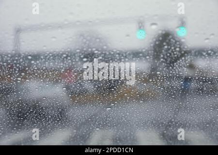 Regentropfen auf einem Fenster mit einer sanft verschwommenen Stadtlandschaft dahinter, die eine stimmungsvolle, atmosphärische Szene erzeugen. Ideal für Wetter, melancholische, gemütliche Momente in Innenräumen, Stockfoto