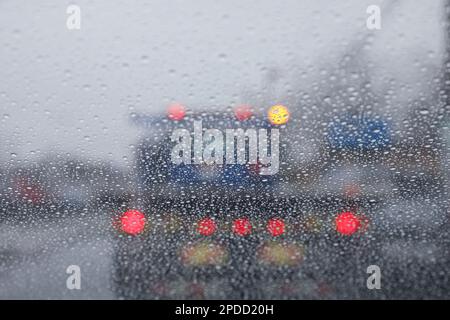 Regentropfen auf einem Fenster mit einer sanft verschwommenen Stadtlandschaft dahinter, die eine stimmungsvolle, atmosphärische Szene erzeugen. Ideal für Wetter, melancholische, gemütliche Momente in Innenräumen, Stockfoto
