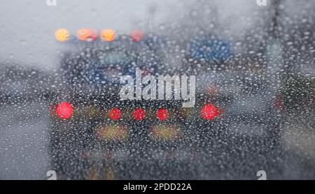 Regentropfen auf einem Fenster mit einer sanft verschwommenen Stadtlandschaft dahinter, die eine stimmungsvolle, atmosphärische Szene erzeugen. Ideal für Wetter, melancholische, gemütliche Momente in Innenräumen, Stockfoto