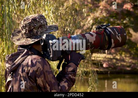 Tokio, Japan - 23. November 2020: Ein Fotograf mit seiner Ausrüstung macht Fotos von Zugvögeln in der Nähe des Teichs im Shinjuku Gyoen Park Stockfoto