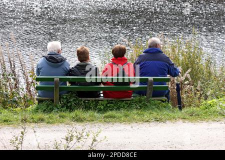 Vier Wanderer sitzen auf einer Bank am Ufer Stockfoto