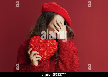 Fröhlichen Valentinstag. Traurige, elegante 40-jährige Frau in rotem Pullover und Baskenmütze mit rotem Herzen. Stockfoto