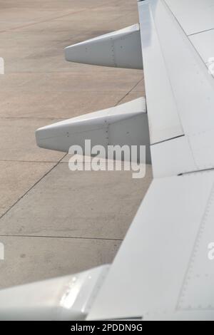 Detail eines Flügels eines geparkten gewerblichen Passagierflugzeugs, Blick aus einem Fenster. Minimalistisches Bild für das Reisekonzept. Stockfoto