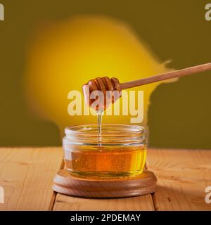 Honig wird von einem Nieselstock in ein Glasgefäß auf einen Holztisch geschossen. Stockfoto