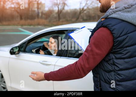 Ausbilder in der Nähe des Fahrzeugs mit seinem Schüler während der Prüfung auf der Fahrschule-Teststrecke Stockfoto