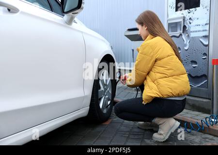 Junge Frau, die beim Autoservice Reifen aufpumpt Stockfoto