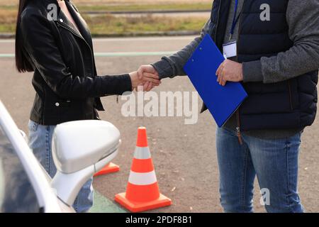 Junge Frau mit Ausbilderin in der Nähe des Autos auf der Teststrecke, Nahaufnahme. Fahrschulprüfung Stockfoto