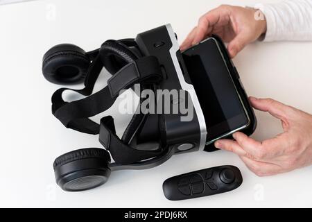 VR-Brille und Smartphone mit Beschneidungspfad für Bildschirm auf weißem Hintergrund. Die Hände von Männern stecken ein Smartphone in eine VR-Brille. Stockfoto