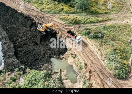 Der Bagger lädt Erde in einen Lkw auf einer Baustelle zur Bodenverbesserung. Drohnenfoto. Stockfoto