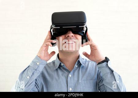 Junger lächelnder Mann mit T-Shirt und Virtual-Reality-Headset oder VR-Brille, der Videospiele spielt, auf weißem Hintergrund Stockfoto