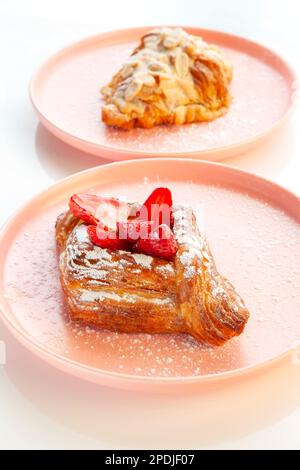 erdbeergebäck auf einem rosafarbenen Teller mit Mandelcroissant im Hintergrund. Stockfoto