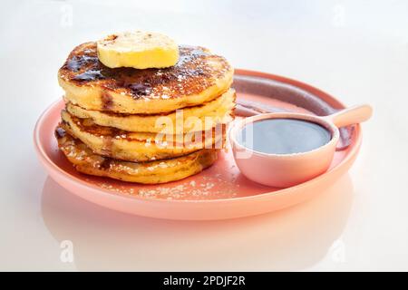 Ein Stapel Blaubeerpfannkuchen, garniert mit Wabenbutter und Ahornsirup auf einem rosa Teller. Stockfoto