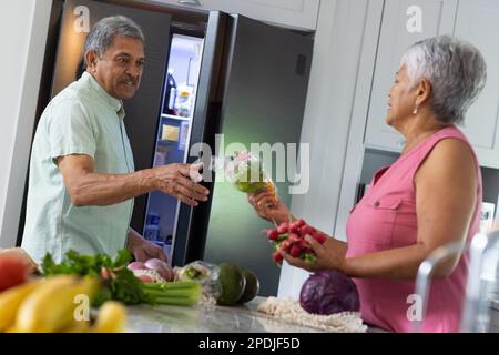 Birassische Seniorin, die ihrem Mann frisches Gemüse gibt, weil sie in der Küche im Kühlschrank aufbewahrt wird Stockfoto