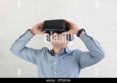 Junger Mann in legerer Atmosphäre mit VR-Brille, berührt etwas Unsichtbares im Kopierraum, Millennials erleben ein Virtual-Reality-Abenteuer auf grauem Backgr Stockfoto