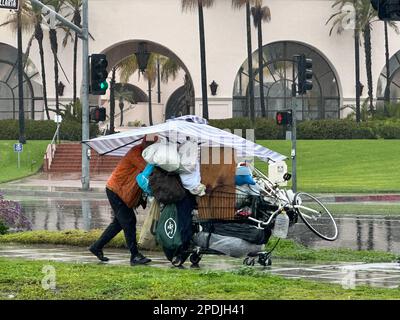 Santa Barbara, Kalifornien, USA. 14. März 2023. Ein obdachloser Mann läuft mit einem riesigen Regenschirm mit Streifen, die zum Querweg auf dem Cabrillo Blvd passen, entlang der Küste von Santa Barbara. Am 14. März 2023 wurde ein Großteil des Santa Barbara County während eines atmosphärischen Sturms evakuiert, der zwölf Stunden lang Regen ohne Pause nach unten ließ. Hier mussten Menschen, die normalerweise auf der Straße oder an den Stränden und Parks von Santa Barbara schlafen und nirgendwo hingehen konnten, umziehen, um überschwemmtes Gras oder sandige Bereiche zu vermeiden, und mussten all ihre Habseligkeiten im eisigen Regen wegbringen. (Kreditbild: © Stockfoto