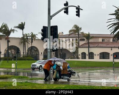 Santa Barbara, Kalifornien, USA. 14. März 2023. Ein obdachloser Mann läuft mit einem riesigen Regenschirm mit Streifen, die zum Querweg auf dem Cabrillo Blvd passen, entlang der Küste von Santa Barbara. Am 14. März 2023 wurde ein Großteil des Santa Barbara County während eines atmosphärischen Sturms evakuiert, der zwölf Stunden lang Regen ohne Pause nach unten ließ. Hier mussten Menschen, die normalerweise auf der Straße oder an den Stränden und Parks von Santa Barbara schlafen und nirgendwo hingehen konnten, umziehen, um überschwemmtes Gras oder sandige Bereiche zu vermeiden, und mussten all ihre Habseligkeiten im eisigen Regen wegbringen. (Kreditbild: © Stockfoto