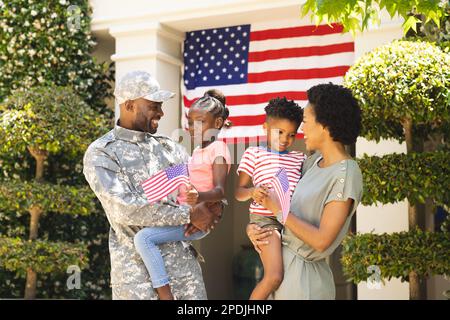 Ein glücklicher afroamerikanischer Soldat und seine Familie umarmen sich und halten usa-Flaggen Stockfoto