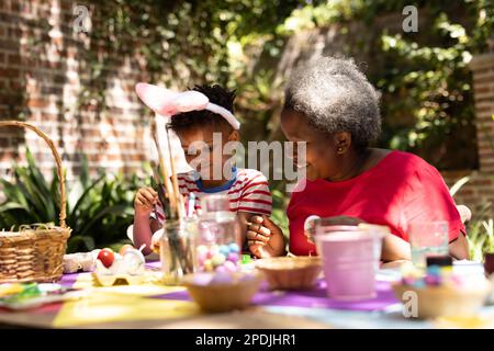 Frohe afroamerikanische Großmutter und Enkel, die ostereier im Garten färbten Stockfoto