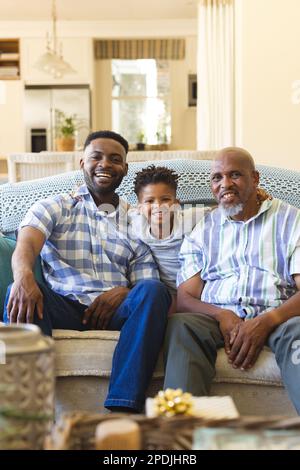 Porträt von glücklichem afroamerikanischen Großvater, Vater und Sohn, die auf dem Sofa im Wohnzimmer sitzen Stockfoto