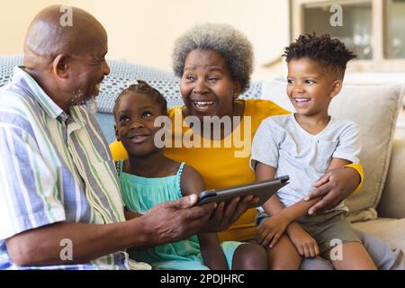 Glückliche afroamerikanische Großeltern und Enkel, die auf dem Sofa sitzen und ein Tablet benutzen Stockfoto