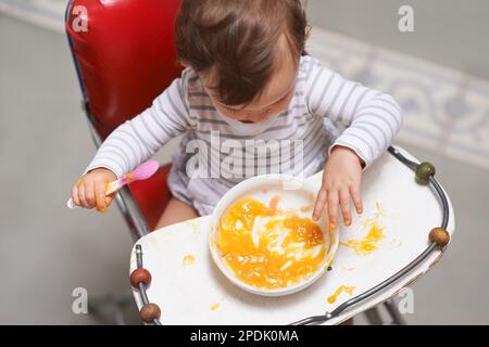 Neue Geschmacksrichtungen entdecken. Ein süßes kleines Baby, das im Hochstuhl sitzt und isst. Stockfoto