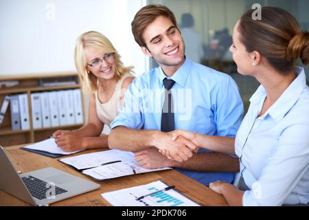 Die Zahlen sehen gut aus. Ein Foto von zwei Kollegen, die sich die Hand schütteln, während ein anderer sie ansieht. Stockfoto
