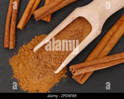 Draufsicht auf Zimtstangen und Gewürzlöffel mit Zimtpulver auf schwarzem Schieferhintergrund Stockfoto