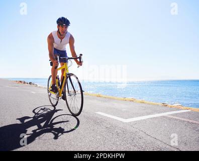 Genießen Sie die Landschaft beim Training. Beschnittene Ansicht eines Radfahrers, der entlang einer Meeresstraße radelt. Stockfoto