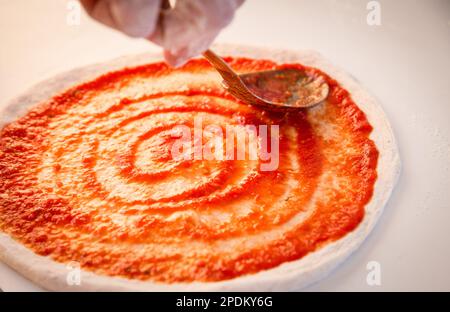 Verteilen Sie Marinara auf einer Pizza, bevor Sie Käse hinzufügen Stockfoto