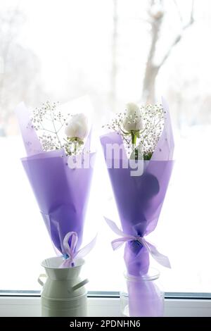 Zwei Sträuße weißer Rosen in lila Verpackung auf der Fensterbank Stockfoto