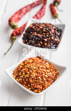 Trockene Chili-Pfefferflocken. Zerdrückte rote Paprika in der Schüssel auf dem weißen Tisch. Stockfoto
