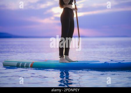 Niedriger Teil einer Surferin, die bei Sonnenaufgang auf dem Surfbrett auf dem See paddelt, niedriger Bereich. Stockfoto