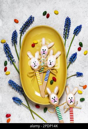 Blick auf handgemachte, farbenfrohe Häschen aus Holzlöffeln auf gelbem Teller. Kleines Geschenk oder Einrichtung zu Ostern. Einfaches, unterhaltsames Bastelkonzept für Kinder. Stockfoto
