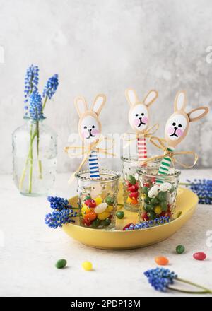 Lustige Häschen aus Holzlöffeln in Gläsern mit süßen Süßigkeiten-Eiern. Kleines Geschenk oder Einrichtung zu Ostern. Einfaches, unterhaltsames Bastelkonzept für Kinder. Selektiver Fokus Stockfoto
