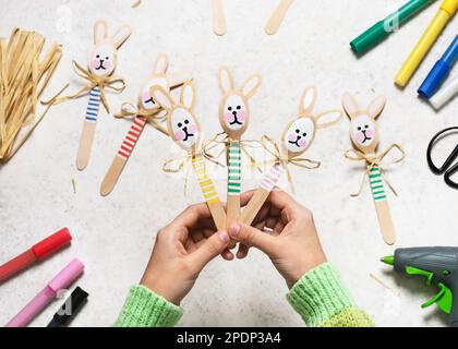 Draufsicht von drei handgemachten bunten Hasen aus Holzlöffeln in Kinderhänden. Kleines Geschenk oder Einrichtung zu Ostern. Einfaches, unterhaltsames Bastelkonzept für Kinder Stockfoto