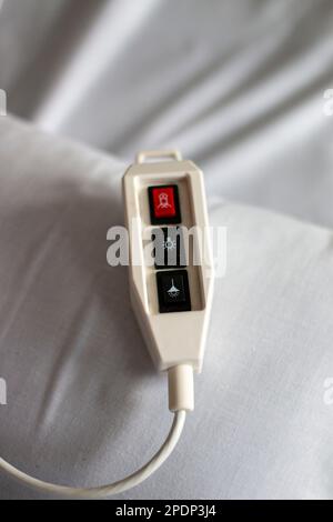 Krankenhausrufsteuerung mit roter Notruftaste, die auf einem Bett mit weißer Bettwäsche ruht Stockfoto